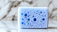 Macro view of blue cleaning sponge with soap bubbles texture on marble background, showing porous structure and foam pattern for household cleaning concept.