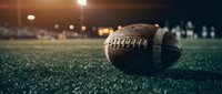American football on green turf field with stadium lights creating dramatic sports atmosphere for game day marketing and athletic promotions.