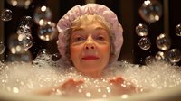 Senior woman with bright smile relaxing in bubble bath with soap foam and floating bubbles, enjoying spa wellness treatment at home in warm atmospheric light.