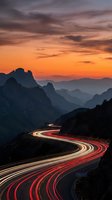 Dramatic mountain highway with light trails at sunset showcasing winding road through scenic landscape with orange purple sky and layered peaks for travel concepts.