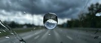 Cracked windshield with circular damage and water droplets during stormy weather conditions creating safety hazard for drivers on rainy day.