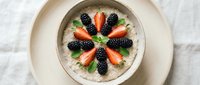 Creamy oatmeal bowl topped with fresh strawberries, blackberries, and mint leaves arranged in a decorative pattern, perfect for breakfast and healthy eating content.