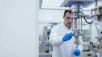 Male scientist in white lab coat and blue gloves operating precision laboratory equipment in modern research facility for pharmaceutical development.
