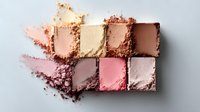 Crushed makeup powder palette in nude and pink tones with soft smudged texture showing color swatches and pigment details on light background.