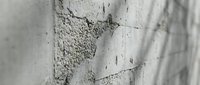 Cracked concrete wall surface showing weathered texture with peeling paint and structural damage in monochrome architectural detail.