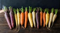 Colorful heirloom carrots in purple, orange, yellow and white varieties arranged in row on rustic wooden background for healthy cooking and farm fresh produce.