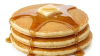 Stack of golden pancakes topped with melting butter and maple syrup, ready for breakfast or brunch dining occasions.