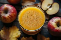 Fresh apple smoothie with cinnamon spice in glass on dark wooden background with whole and cut red apples and autumn maple leaves.