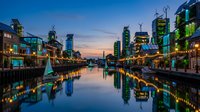 Modern urban waterfront district at twilight with illuminated buildings reflecting in calm river creating stunning cityscape panorama for commercial use.