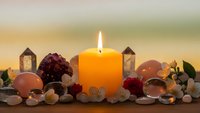 Orange candle burning surrounded by healing crystals, gemstones and flowers creating peaceful meditation and wellness atmosphere for spiritual practices.