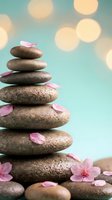 Zen spa stones balanced in pyramid with pink cherry blossom petals on turquoise background with soft bokeh lights for wellness and meditation concepts.