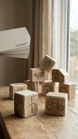Wooden blocks with engraved eco-friendly symbols including leaves, bicycle, and cross arranged on table near window with sustainability brochures and natural curtains for environmental awareness campaigns.