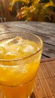 Refreshing iced orange drink in a glass on a wooden table outdoors, with tropical greenery in the background on a sunny day.