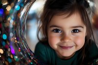 Adorable young girl with brown hair and bright eyes smiling through transparent bubble, wearing green sweater with colorful bokeh lights in background.