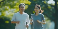 Middle-aged Asian couple jogging together in park during morning workout, wearing casual sportswear and enjoying active lifestyle in natural setting.