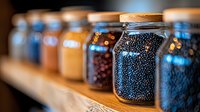 Glass jars filled with colorful spices and dried ingredients on wooden shelf, selective focus on black peppercorns in foreground, creating rustic kitchen pantry atmosphere.