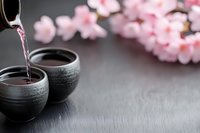 Traditional Japanese sake being poured into ceramic cups with cherry blossoms on dark slate background for cultural dining and celebration concepts.