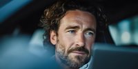Mature Caucasian businessman with beard and curly hair sitting in car interior looking thoughtful and confident during business travel or commute.