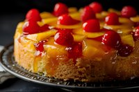 Golden pineapple upside-down cake with glossy red cherries on cooling rack, homemade dessert ready for serving at bakery or restaurant kitchen.