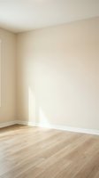 Empty room corner with beige walls and light wood laminate flooring for interior design and real estate projects.