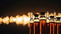Row of amber glass vials with cork stoppers containing liquid samples against warm bokeh lights background for pharmaceutical research and laboratory work.