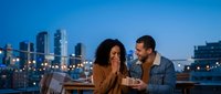 Young couple enjoying romantic evening date on rooftop terrace with city skyline backdrop during blue hour twilight for lifestyle and relationship content.