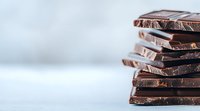 Stack of broken dark chocolate pieces arranged in layers with soft focus background, showcasing rich texture and glossy surface for culinary and dessert designs.