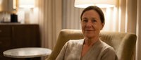 Smiling senior Caucasian woman relaxing in comfortable armchair at home, warm evening lighting creating cozy atmosphere for retirement lifestyle content.