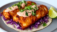 Crispy beer-battered fish tacos with spicy mayo sauce, fresh cilantro and purple cabbage slaw on corn tortillas served with lime wedges for Mexican cuisine.