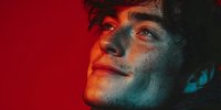 Young man with freckles illuminated by dramatic red and blue lighting, creating a moody atmospheric portrait against vibrant background.