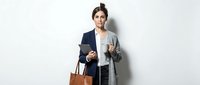 Professional businesswoman in elegant coat holding coffee and bag against white background for corporate lifestyle concepts.