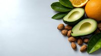 Fresh avocado halves, oranges, almonds and green leaves arranged on light background with copy space, healthy food ingredients for breakfast.