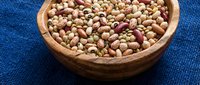 Mixed legumes and beans in wooden bowl on blue textile background for healthy cooking and nutrition concepts.