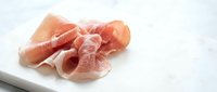 Thin slices of cured ham arranged on white plate, delicate prosciutto meat for gourmet cooking and appetizer preparation in culinary presentations.