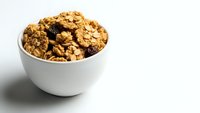 Homemade granola with oats, nuts and dried fruits in white ceramic bowl on clean background for healthy breakfast and snacking concepts.