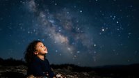 Young child with curly dark hair gazing upward at starry night sky with milky way galaxy visible, expressing wonder and awe at cosmos for astronomy, education, and inspiration concepts.