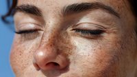 Close-up portrait of young woman with freckles and closed eyes against blue background, showcasing natural beauty and peaceful expression.