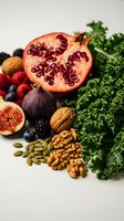Fresh superfood collection with pomegranate, kale, berries, nuts and figs arranged on white background for healthy eating and nutrition concepts.