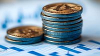 Stack of golden and silver coins on financial chart background showing market data and business growth analysis for investment decisions.