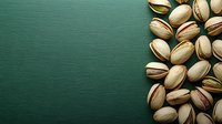 Roasted pistachio nuts scattered on green textured background with copy space for healthy snacking and culinary designs.
