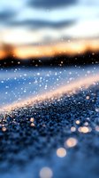 Magical winter scene with sparkling snow crystals glowing at sunset, creating dreamy bokeh effect against blurred blue and orange sky background.