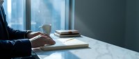 Professional businessman reading book at modern office desk with coffee cup during morning work routine for productivity and learning.