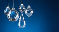 Elegant crystal glass ornaments hanging on silver chains against deep blue background for luxury holiday decoration and festive seasonal display.