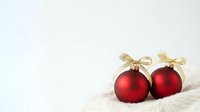 Pair of red matte ornaments with gold ribbon bows on white knit fabric background, suitable for holiday greeting cards, seasonal marketing, and festive decorations.
