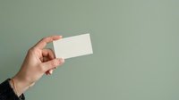 Female hand holding blank white business card against sage green background for branding and corporate identity mockup purposes.