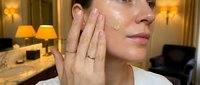 Young Caucasian woman applying facial cream in luxury hotel room with golden lighting for skincare routine and beauty treatment.