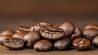 Fresh roasted coffee beans scattered on wooden surface with selective focus, showing rich brown color and natural texture in macro photography.