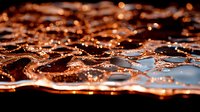 Mesmerizing copper-toned liquid surface with ripples and waves creating abstract patterns, illuminated by warm light against dark background. Macro photography.