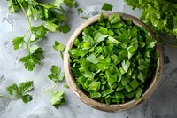 Fresh chopped parsley leaves in rustic ceramic bowl on gray concrete background, scattered herbs around, overhead view for cooking and garnishing.
