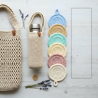 Eco-friendly crocheted accessories set with reusable cotton pads, shopping bags and bottle holder for sustainable zero waste lifestyle on white wood.